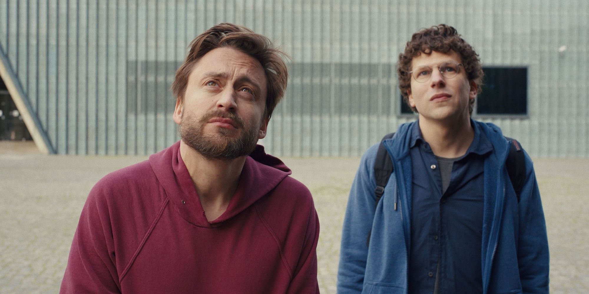 Kieran Culkin and Jesse Eisenberg stare up at a statue in Poland in A Real Pain