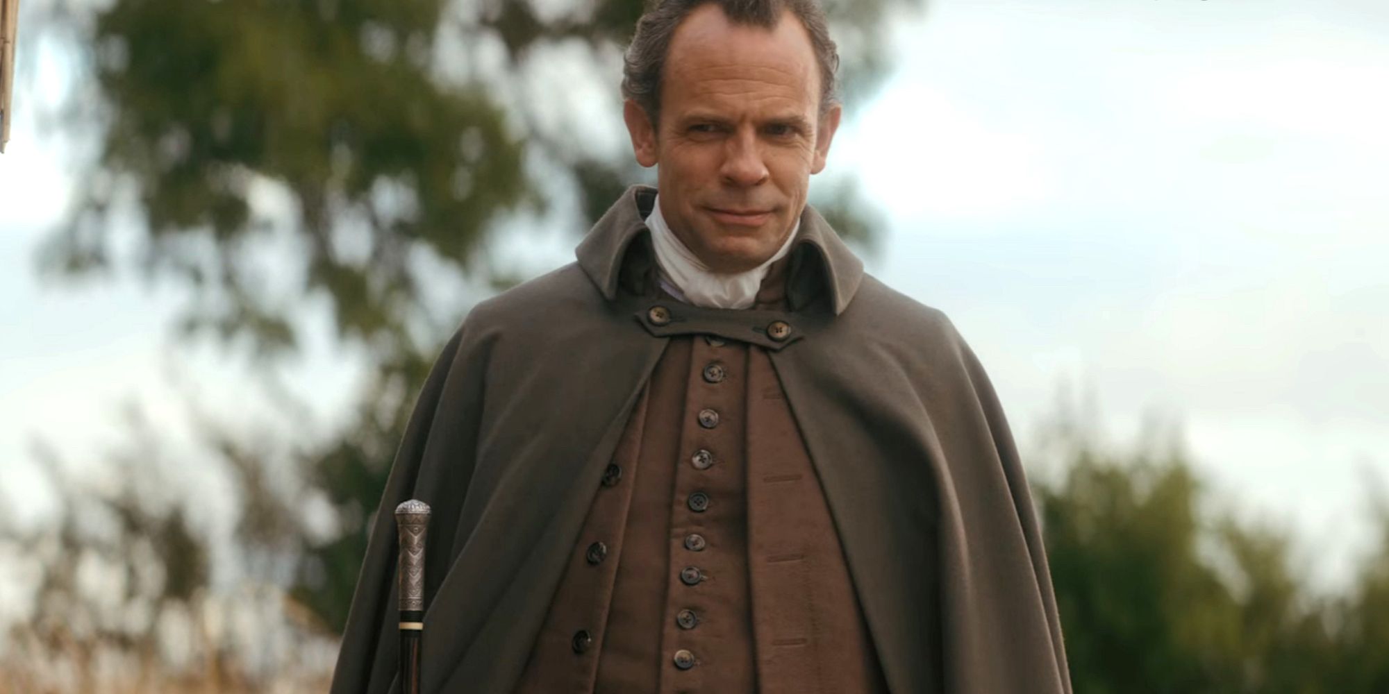 Keir Charles as Lord Ledger stands in front of a tree in Queen Charlotte: A Bridgerton Story