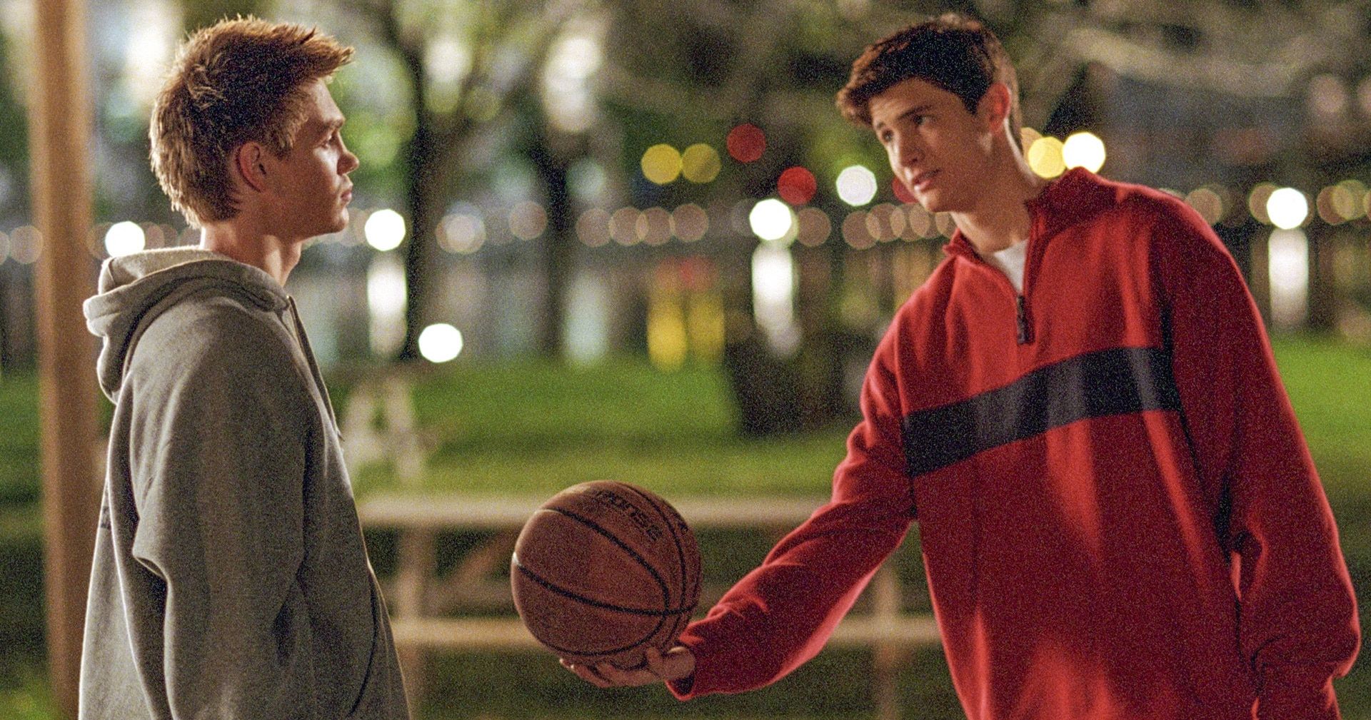 Nathan (James Lafferty) hands Lucas a basketball at the River Court on One Tree Hill.