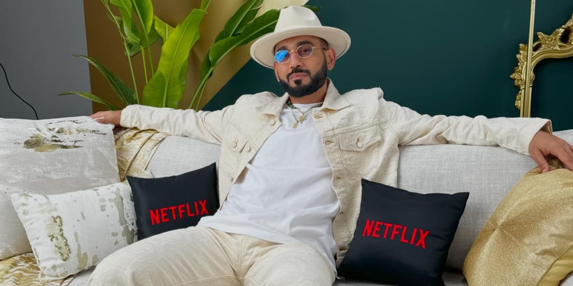 Dubai Bling Dj Bliss sitting on a sofa with black Netflix pillows next to him