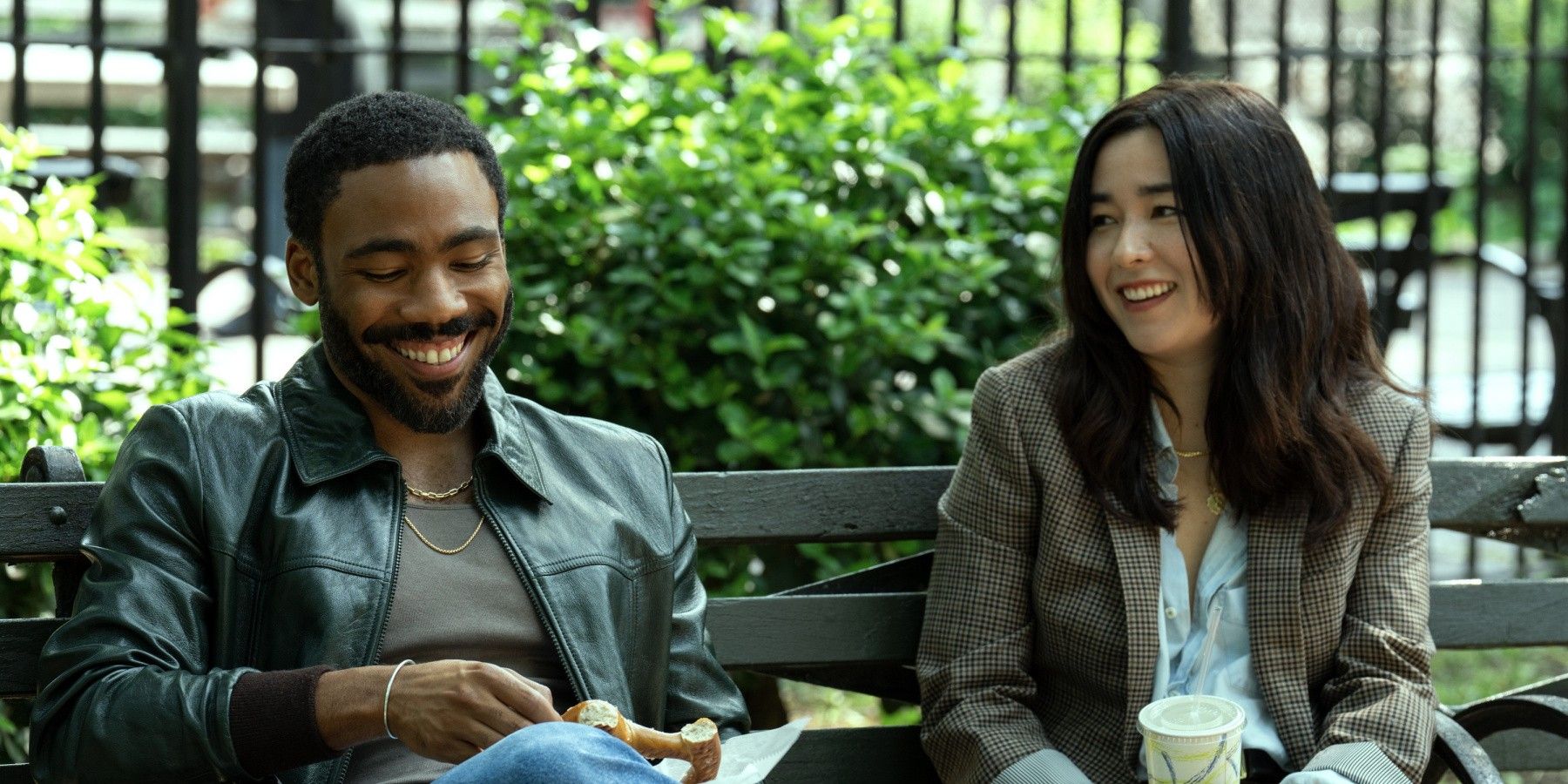 Donald Glover and Maya Erskine laughing on a bench in Mr. & Mrs. Smith