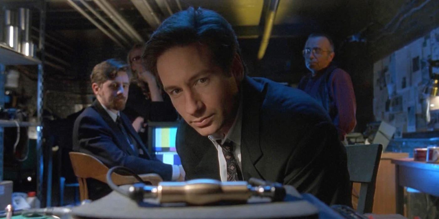 Mulder inspects a piece of evidence while the Lone Gunmen look on in the X-Files