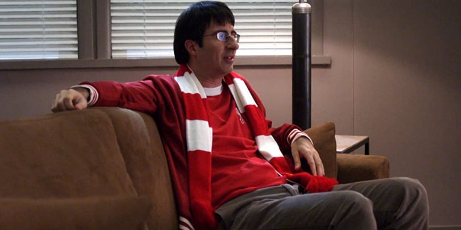 Professor Ian Duncan Sits on a Couch While Wearing a Red Shirt and Red and White Striped Scarf in Community