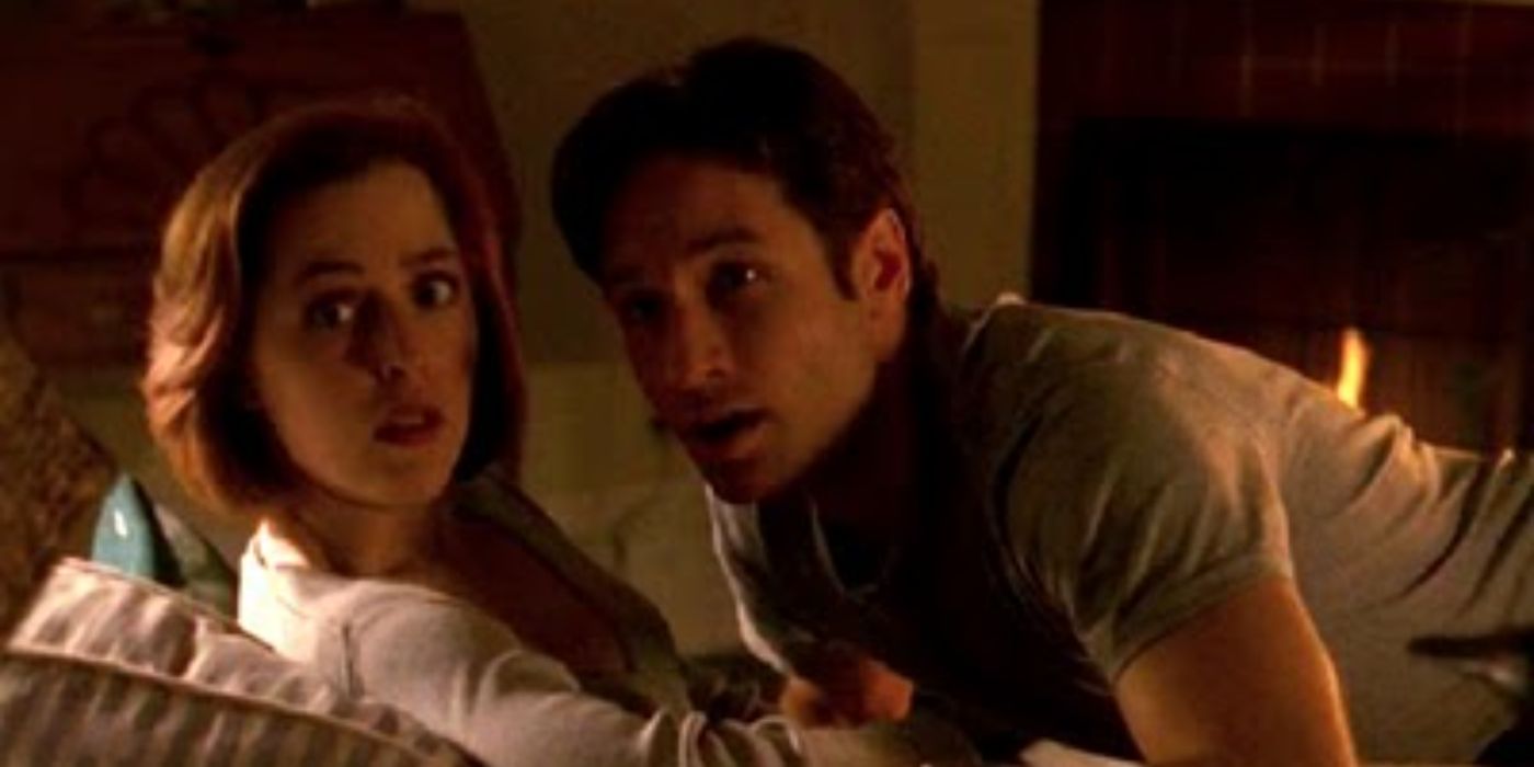 Scully and Mulder looking behind them while sitting on a couch in The X-Files