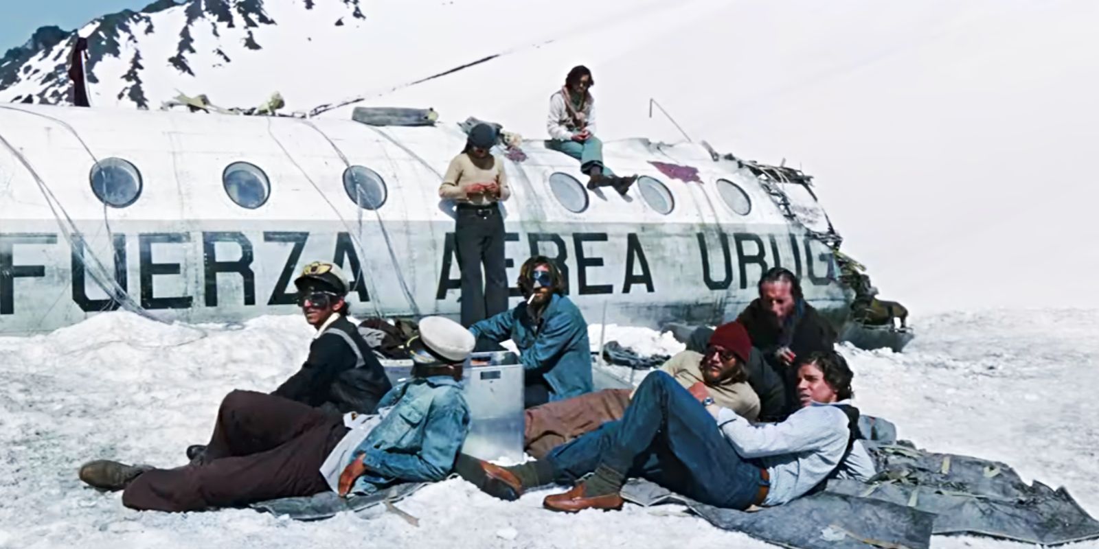 Vários sobreviventes sentados do lado de fora do avião em ruínas na Sociedade da Neve