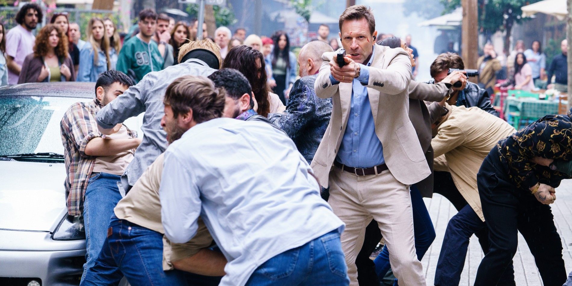 Aaron Eckhart pointing a gun in the middle of a chaotic crowd in The Bricklayer