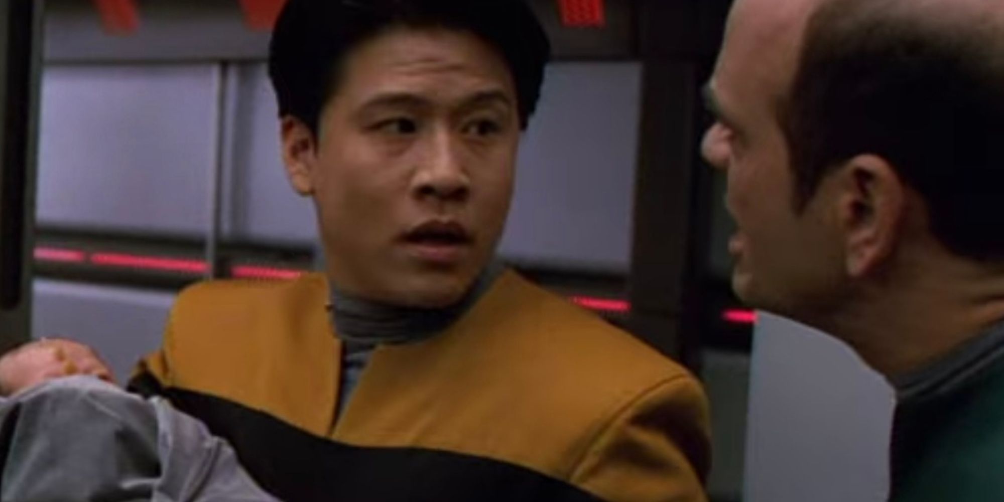 Garrett Wang holding a baby as Harry Kim in Star Trek: Voyager as the EMH talks to him