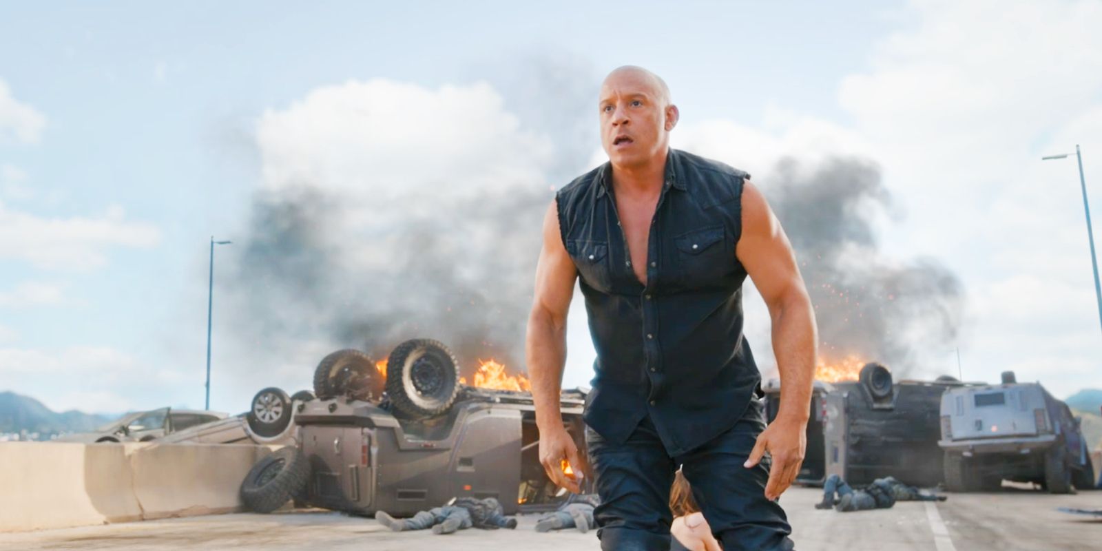 Vin Diesel's Dominic Toretto standing in front of multiple cars on fire in Fast X