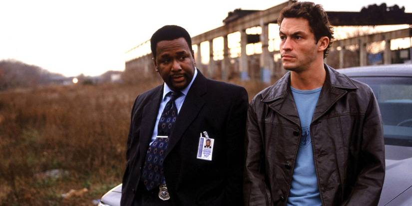 Wendell Pierce as Bunk Moreland and Dominic West as Jimmy McNulty sitting on the hood of their patrol vehicle in The Wire.