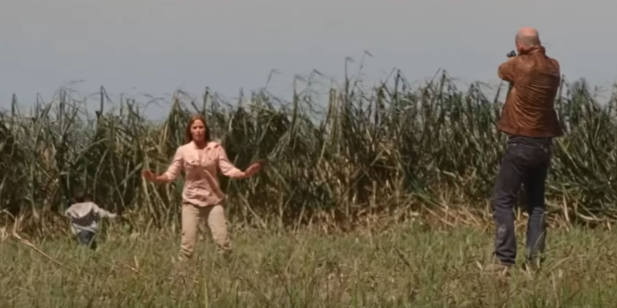 Old Joe aiming a gun at Sara in Looper as Cid escapes into the field behind