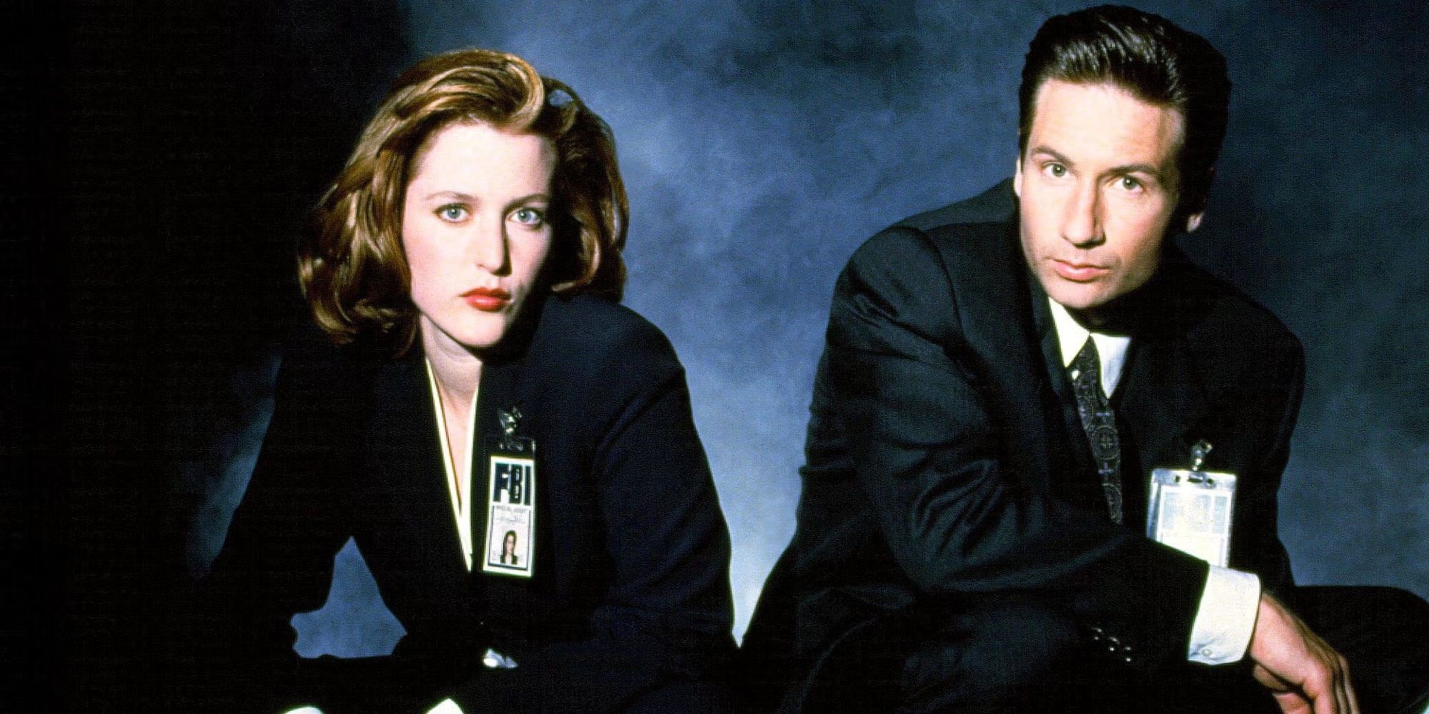 Mulder (Gillian Anderson) and Scully (David Duchovny) kneel in front of a foggy background in a promotional image for The X-Files