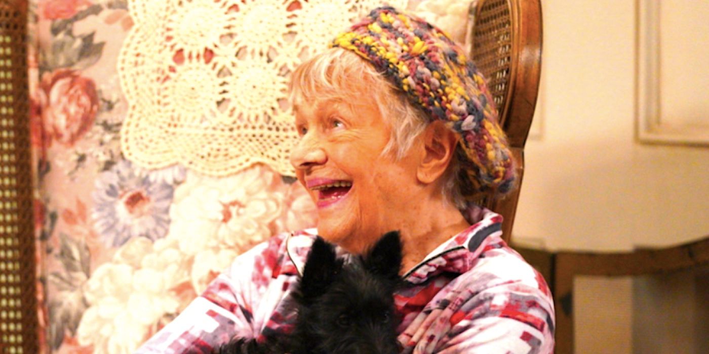 Bev sitting in a chair holding a puppy and laughing in The Conners season 6 episode 2