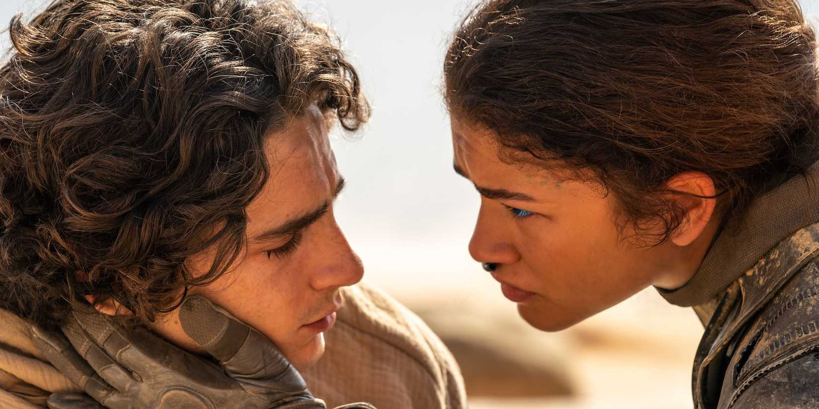 Zendaya as Chani grips Timothee Chalamet as Paul's face as they look at each other while in the Arrakis desert in Dune: Part Two
