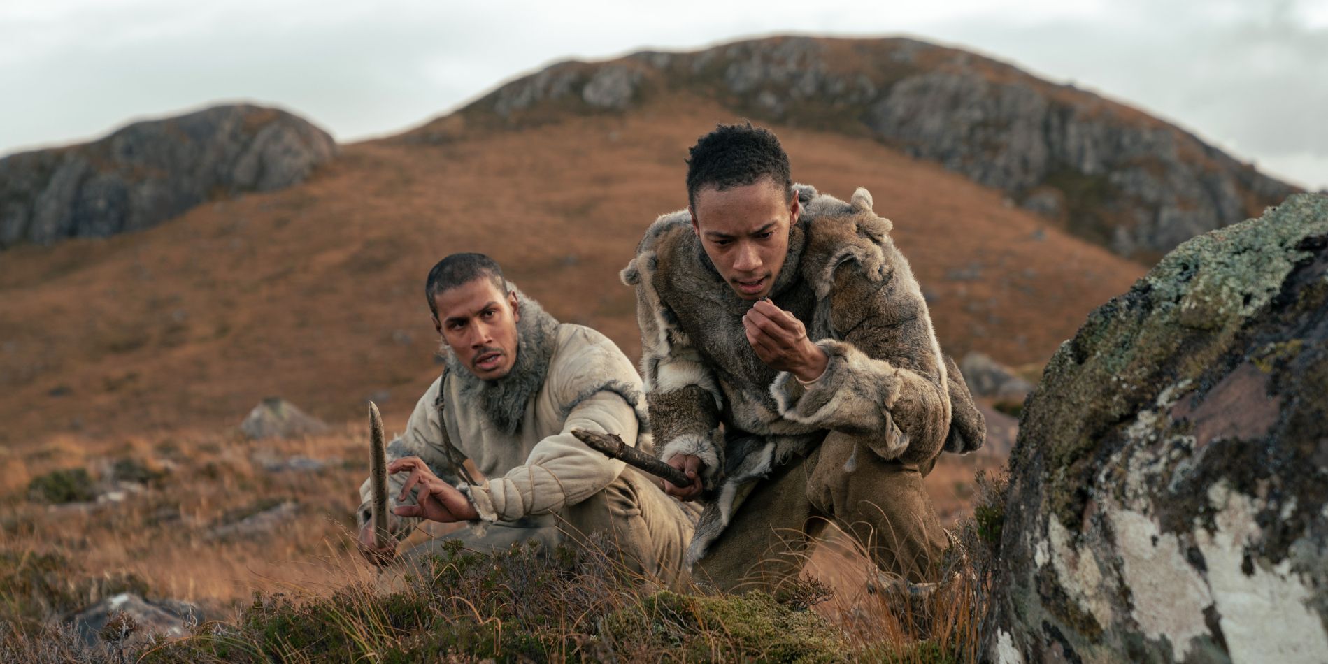 Chuku Modu and Kit Young holding spears and studying the land in Out of Darkness