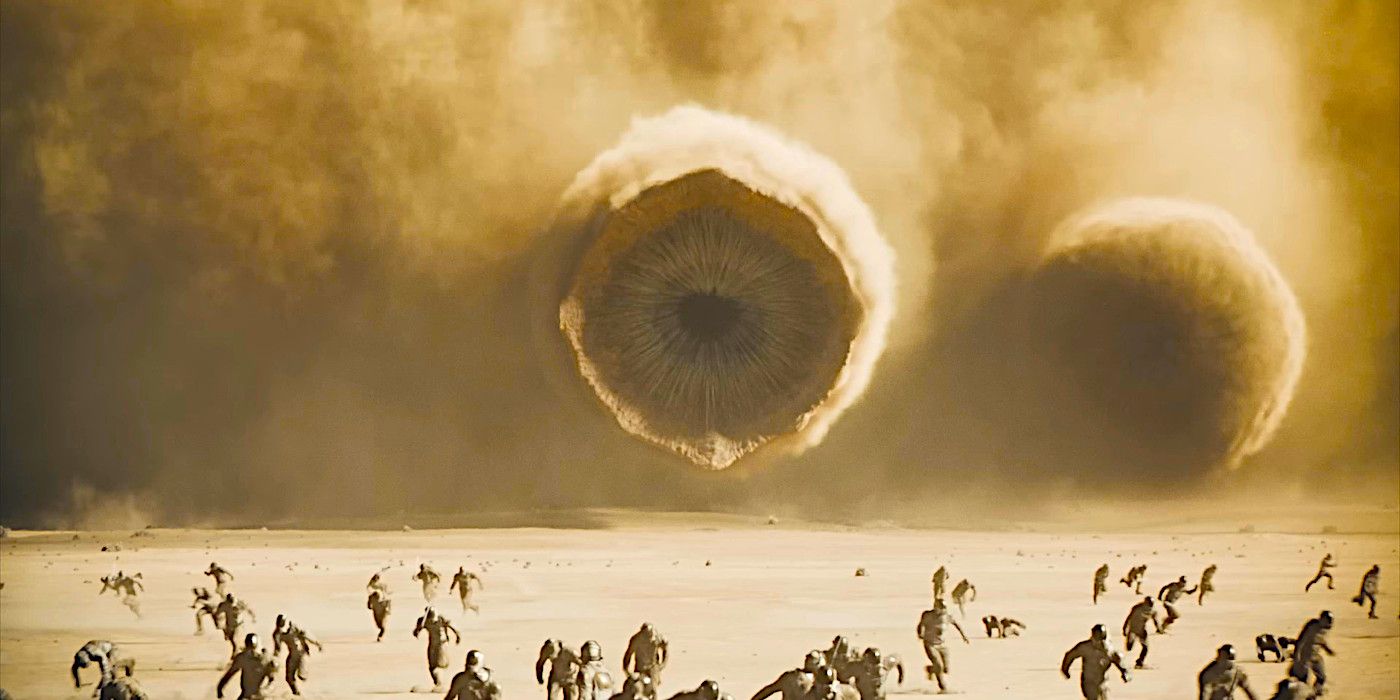 A sandworm emerges from a billowing dust cloud while tiny human figures flee in a dramatic scene from Dune: Part Two
