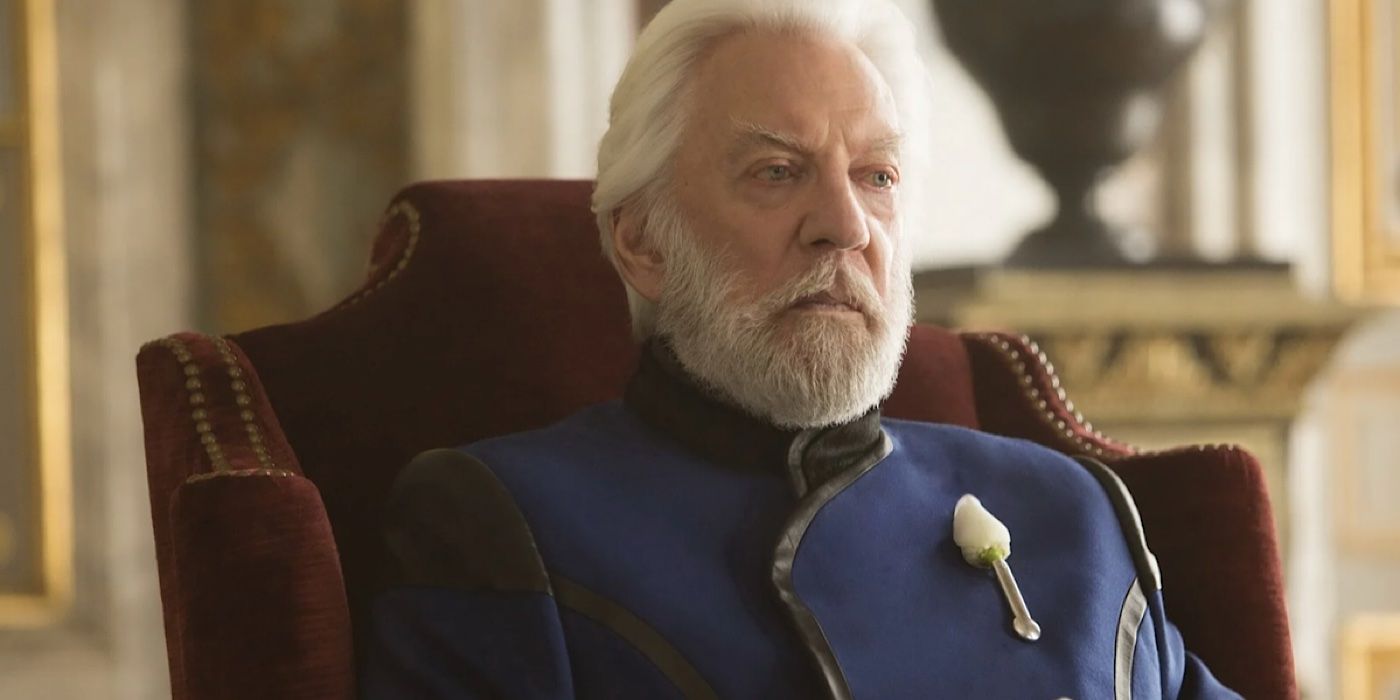 President Snow sits in a chair with a white rose on his jacket in The Hunger Games. 