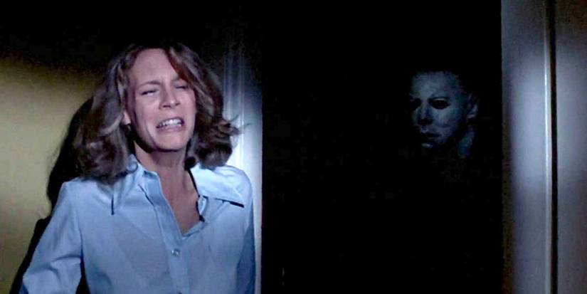 Jamie Lee Curtis as Laurie Strode crying while Nick Castle as Michael Myers lurks in a doorway in Halloween 1978