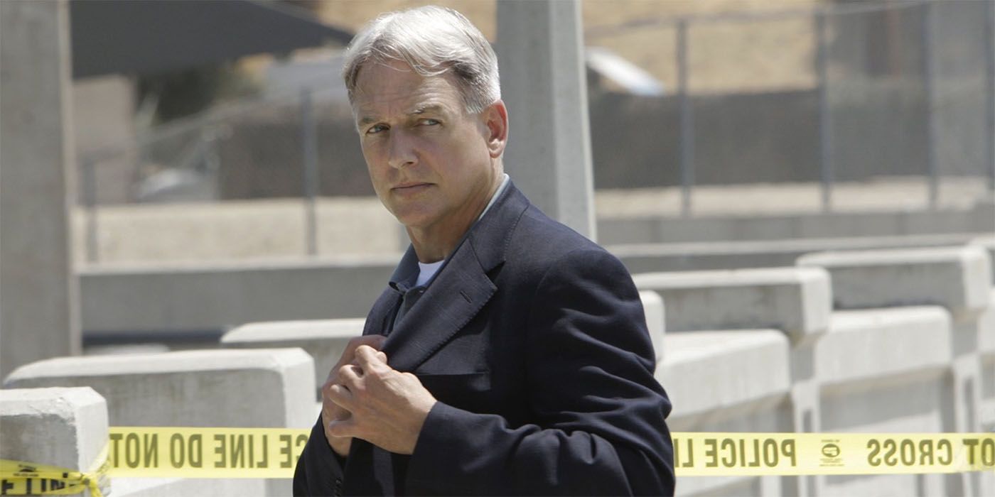Mark Harmon as Gibbs reaching into his jacket pocket with police tape behind him in NCIS