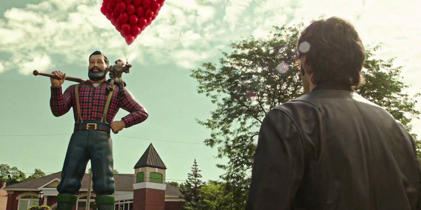 Richie looks up at Pennywise who holds balloons while sitting on the Paul Bunyon statue IT Chapter Two