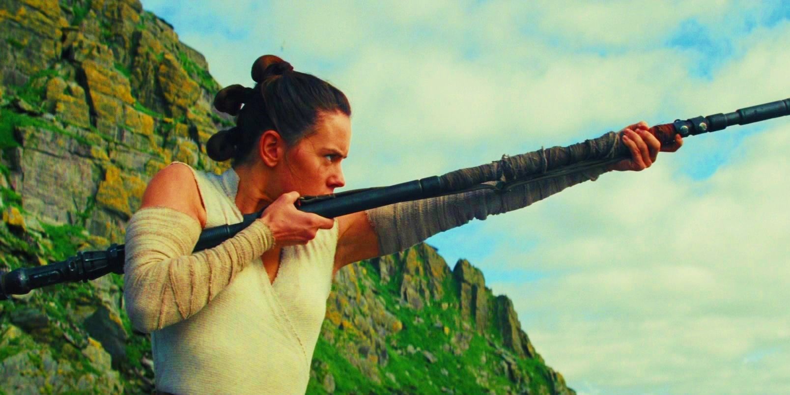 Rey stands with her staff pointed toward the sky in Star Wars: The Last Jedi