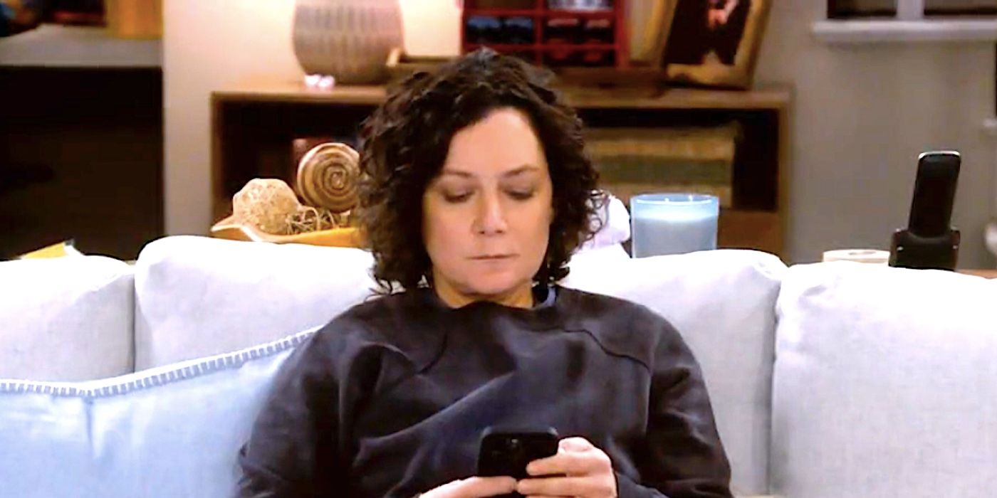 Sara Gilbert's Darlene checks her phone on the couch in The Conners season 6 episode 3