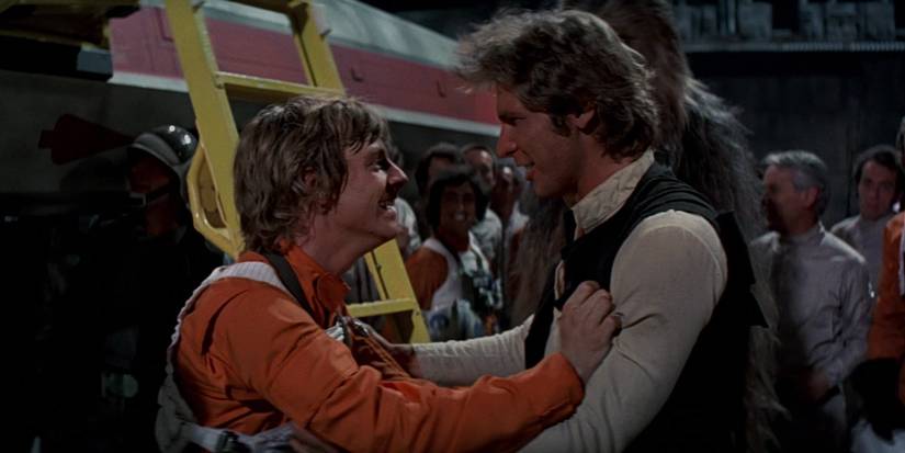 Luke Skywalker (Mark Hamill) and Han Solo (Harrison Ford) celebrate in front of an X-Wing, Chewbacca, and other members of the Rebel Alliance after the destruction of the Death Star in Star Wars: Episode IV - A New Hope