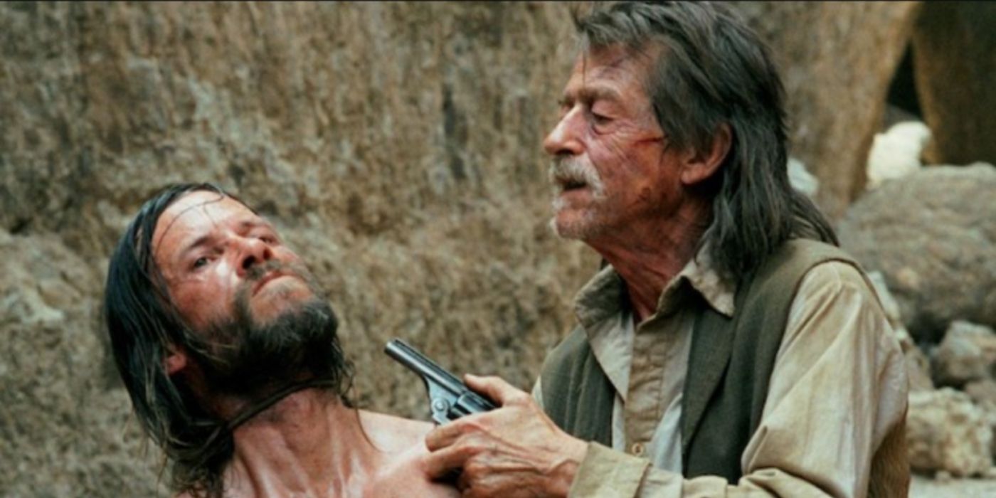 Charlie (Guy Pearce) com uma arma apontada para a cabeça empunhada por Jellon (John Hurt) em A Proposição