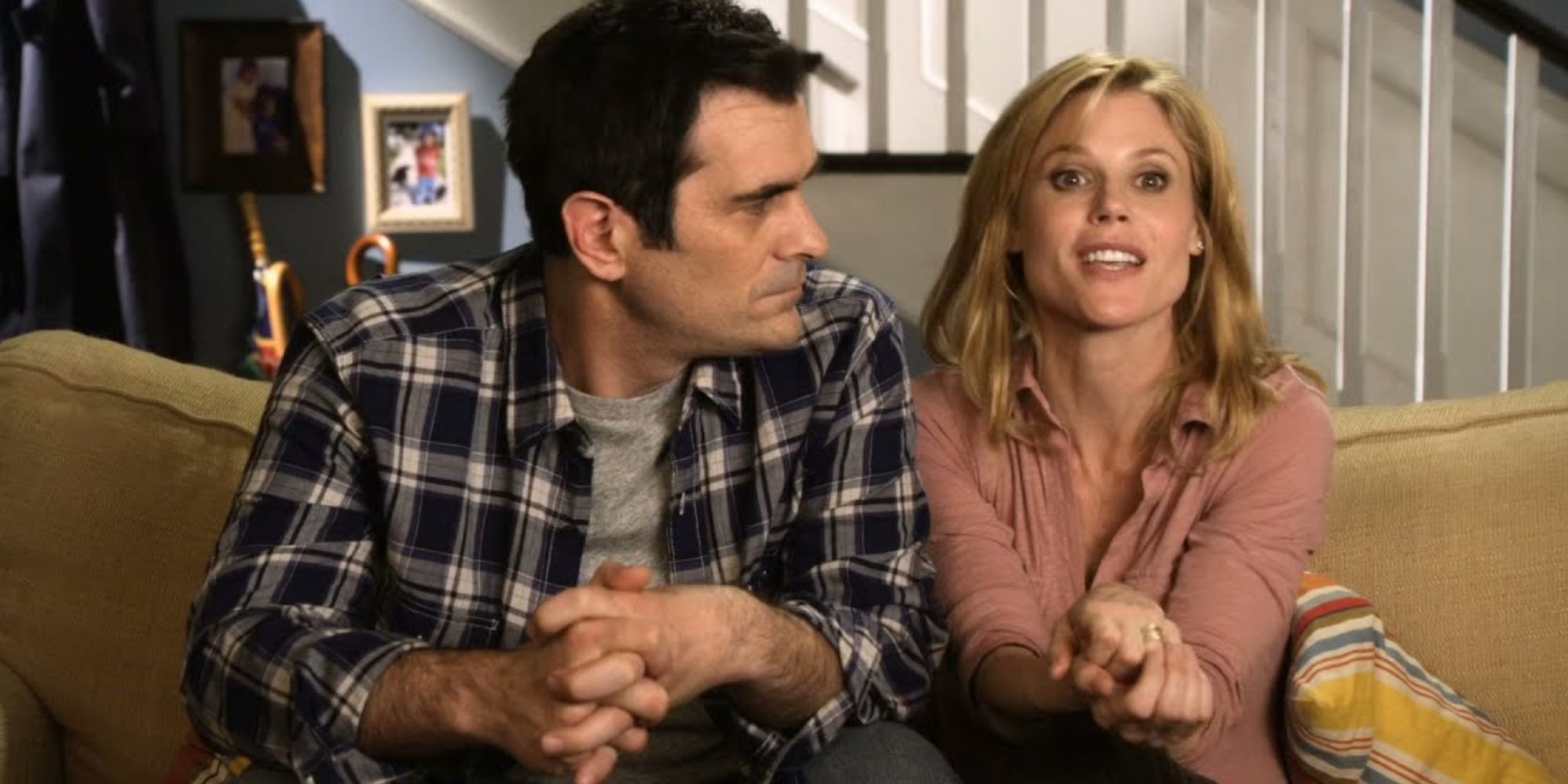 Ty Burrell as Phil Dunphy sitting on a couch and looking at Julie Bowen as Claire Dunphy in Modern Family