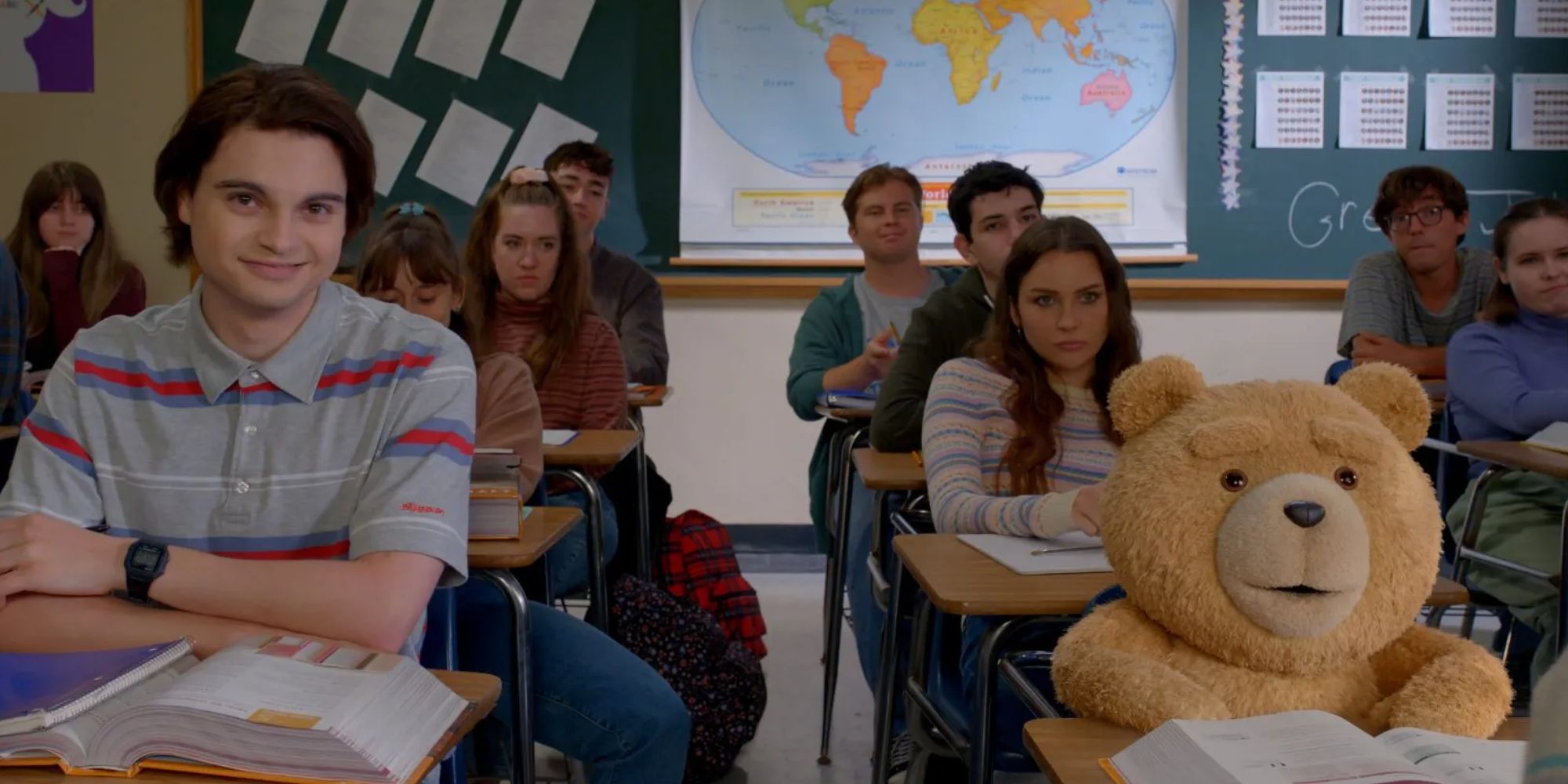 Max Burkholder as John Bennett sits with Ted in a classroom smiling in the Ted TV showMax Burkholder as John Bennett sits with Ted in a classroom smiling in the Ted TV show