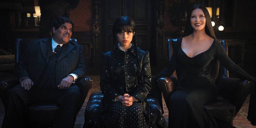 Gomez (Luis Guzmán) and Morticia (Catherine Zeta-Jones) smile as Wednesday (Jenna Ortega) scowls in Principal Weems' office in Wednesday.