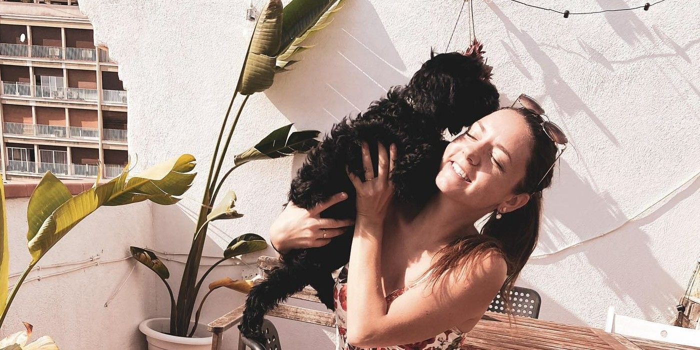 Laura Bileskaline from Below Deck Down Under smiles while cuddling a black dog and wearing a sundress with sunglasses on top of her head.