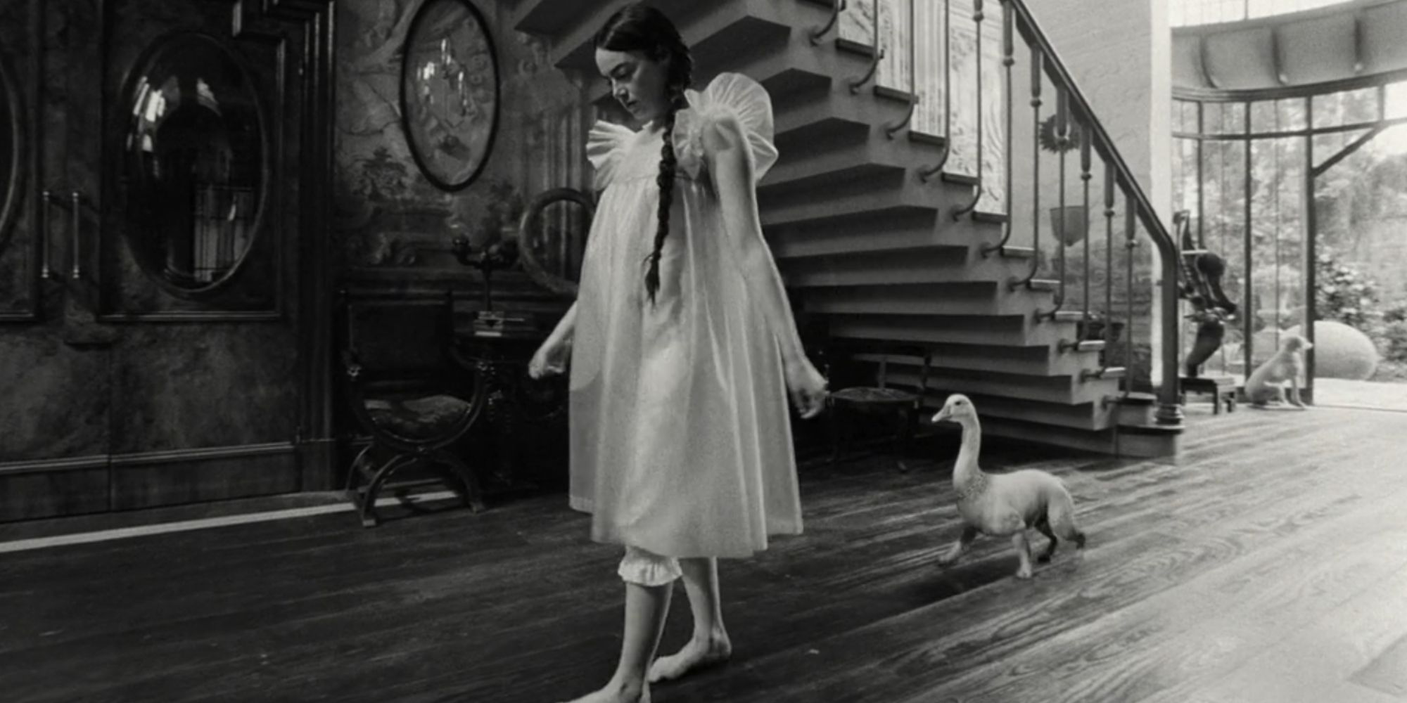 Emma Stone as Bella Baxter in Poor Things walking along in a white dress with a duck/dog hybrid walking behind her