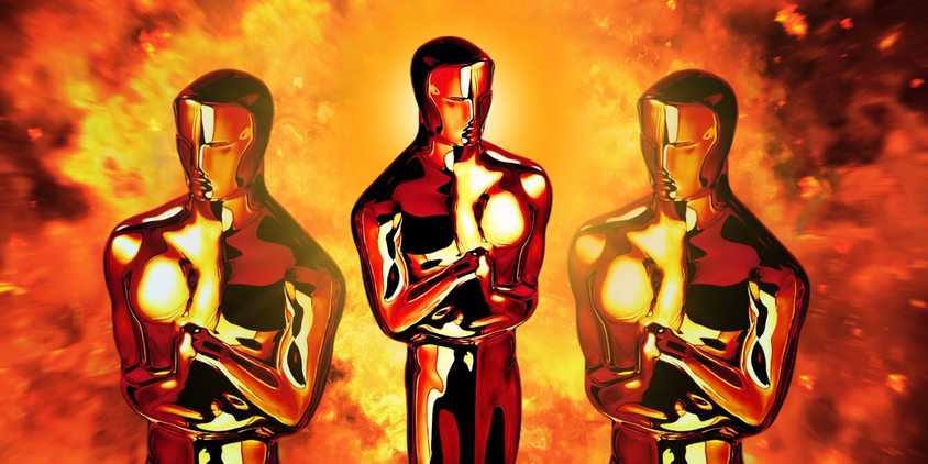 Three Oscar statuettes on top of a fiery background