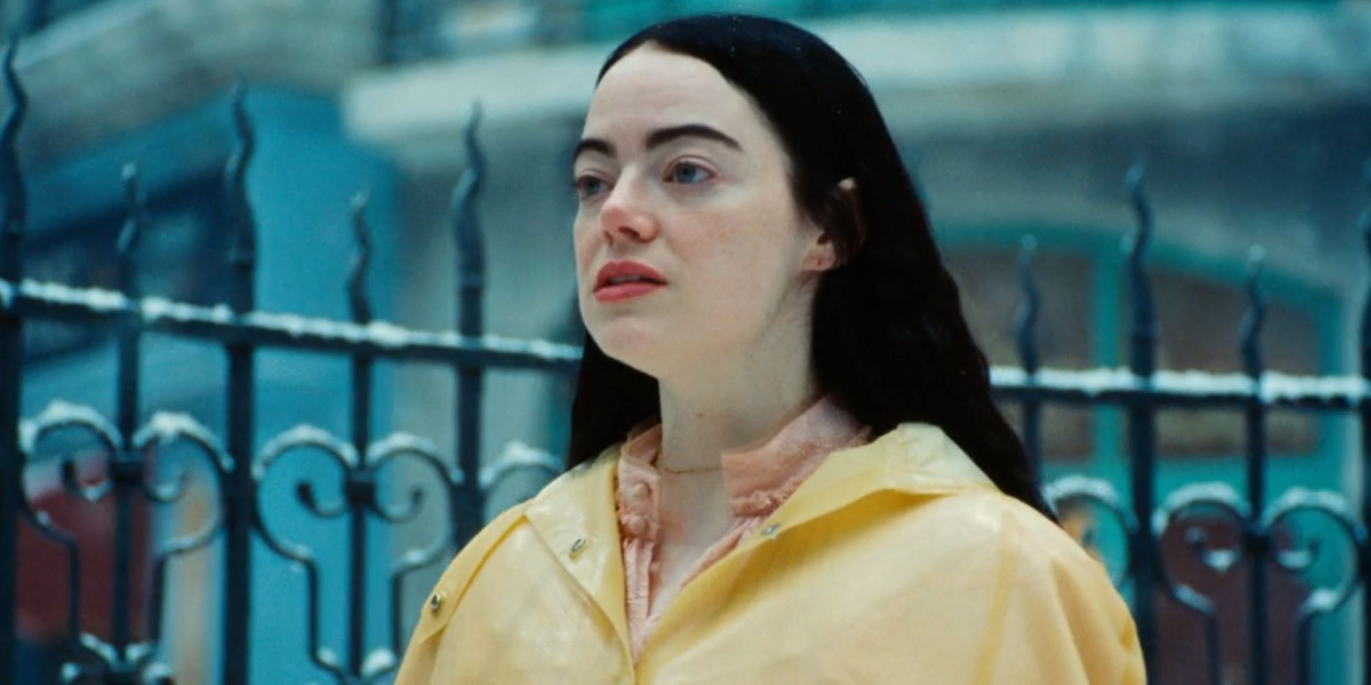 Emma Stone in a yellow coat with a straight face as Bella Baxter in Poor Things