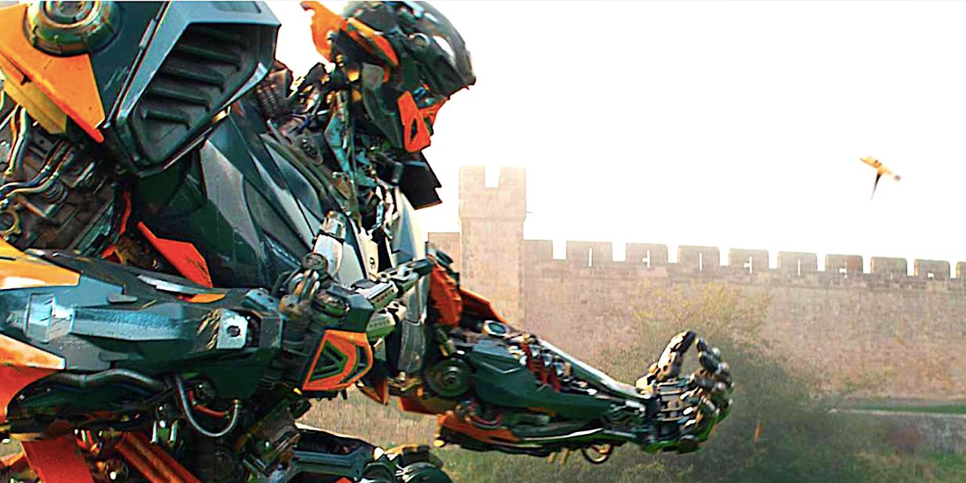 A Transformer stoops down with its hand out beside a castle in Transformers The Last Knight 2017