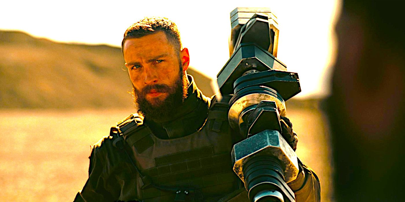 Aaron Taylor-Johnson scowling and holding a large, elongated metallic object hoisted on his shoulder in a scene from Tenet