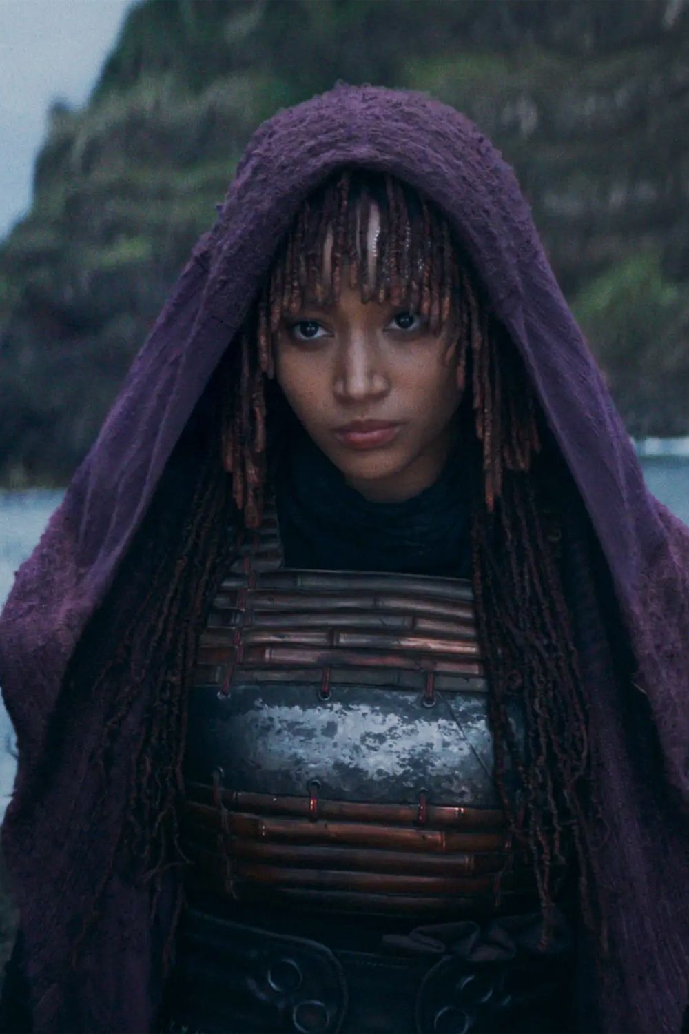 Amandla Stenberg como Mae em Star Wars, o Acólito, vestindo um manto roxo no topo de um penhasco