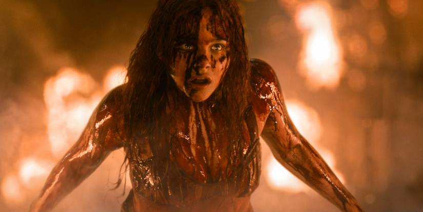 Carrie is covered in blood with flames in the background in Carrie.