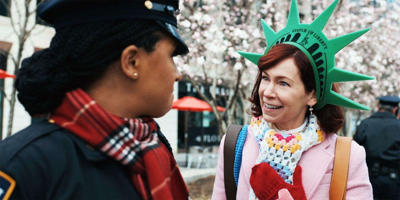 Carrie Preston smiling and wearing a Statue of Liberty hat as Elsbeth in Elsbeth season 1, episode 1
