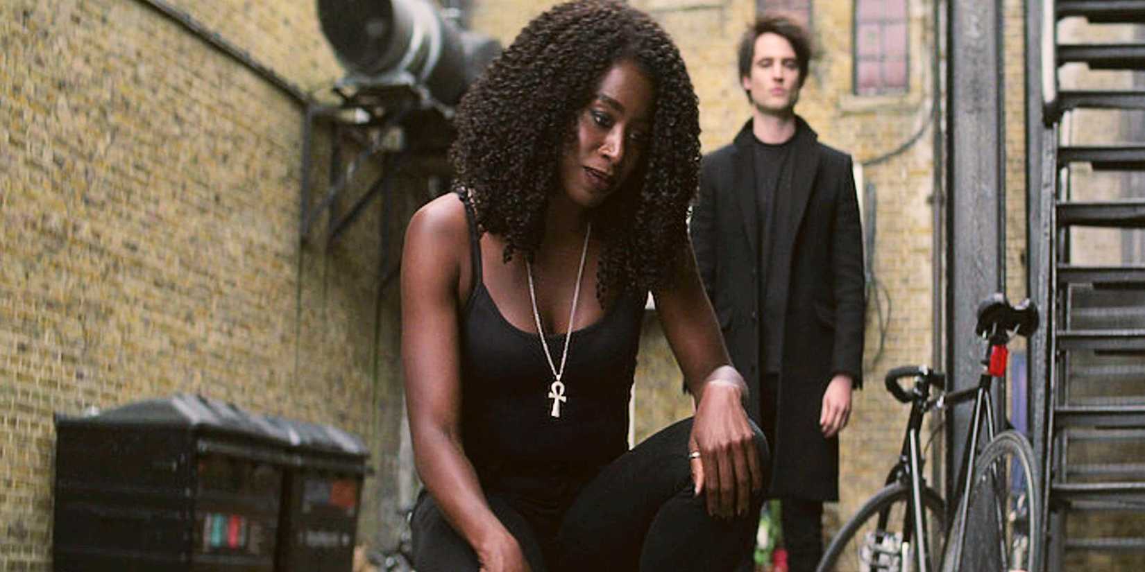 Death kneeling in an alley while Dream stands behind her in The Sandman