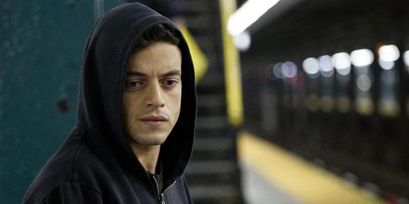 Elliot Alderson has a serious expression on his face while standing in the subway station.