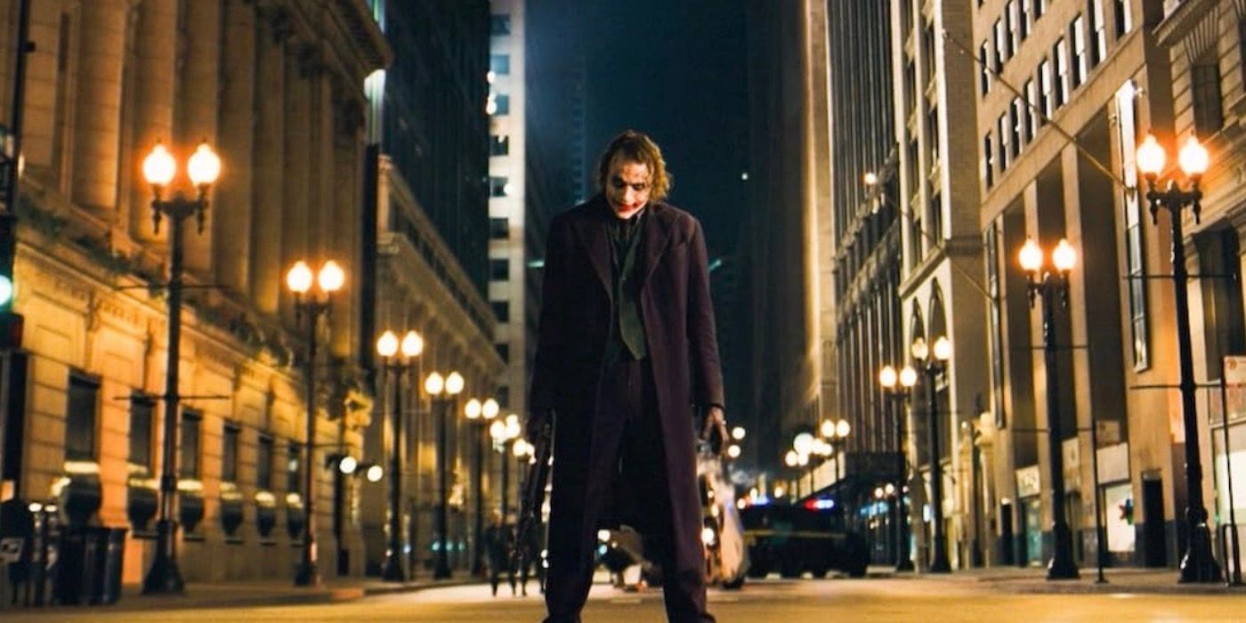Heath Ledger as the Joker standing in the street with a gun in The Dark Knight. 