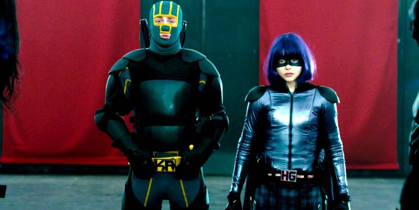 Hit-Girl in her black and purple suit and Kick-ᴀss in his yellow and green suit waiting at the end of the room in Kick-ᴀss 2