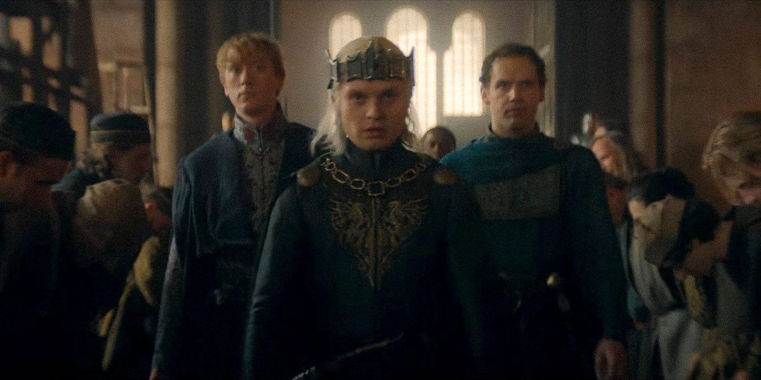 Aegon II Targaryen usando uma coroa escoltado por dois homens enquanto as pessoas se curvam diante dele na 2ª temporada de House of the Dragon