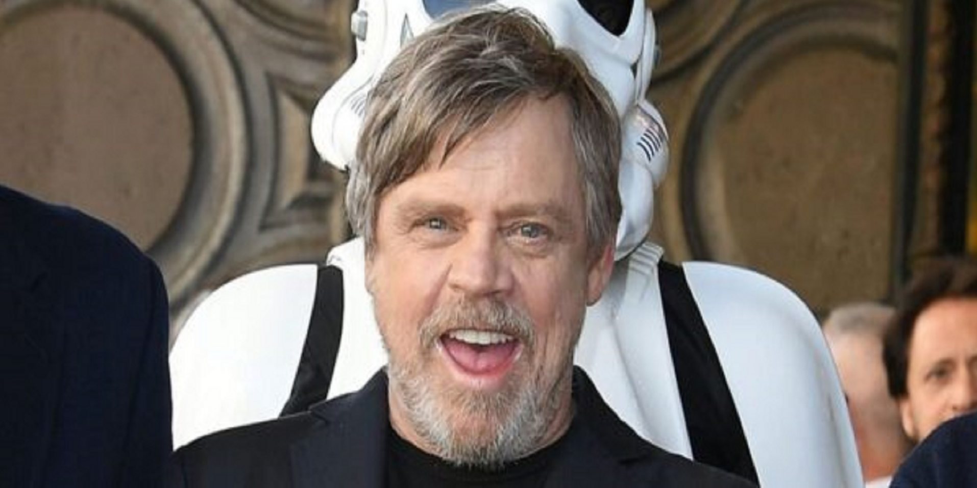 Mark Hamill sorride alla telecamera con uno stormtrooper in piedi dietro di lui