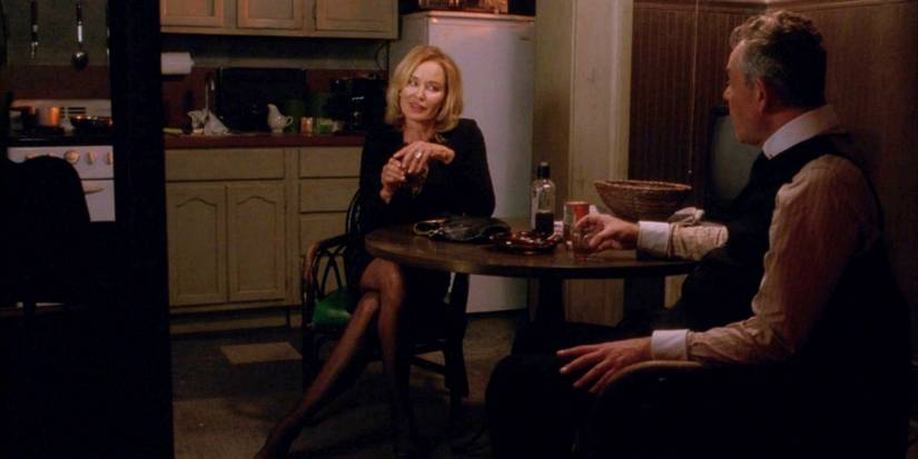Danny Huston as the Axeman of New Orleans and Jessica Lange as Fiona Goode sitting at a table in American Horror Story: Coven