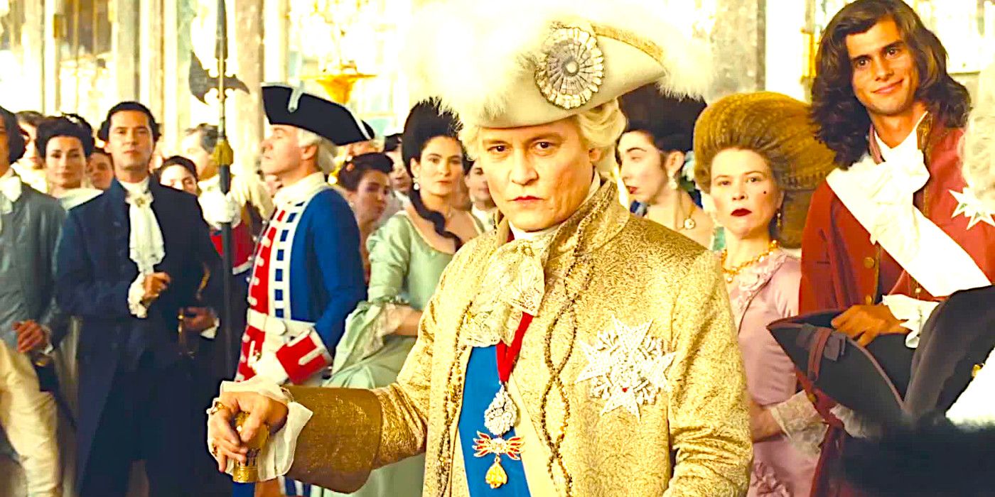 Johnny Depp dressed in 18th Century costume and standing with a cane looking smug amid well-dressed courtiers in a scene from Jeanne du Barry