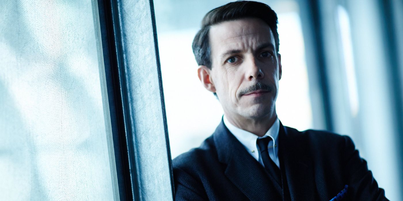 Mr. Robertson (Noah Taylor) leaning against a wall and smiling in Predestination.