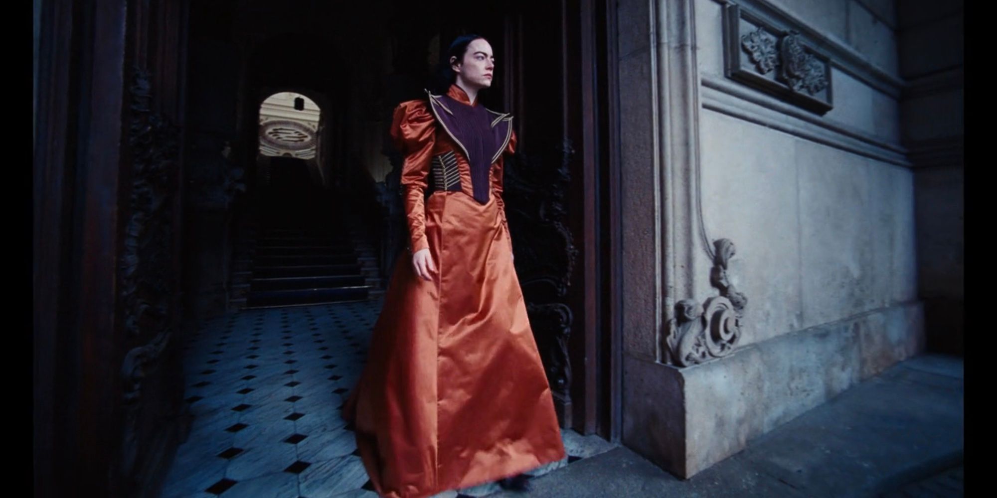 Bella Baxter (Emma Stone) wears an orange satin gown with purple detailing in Poor Things.