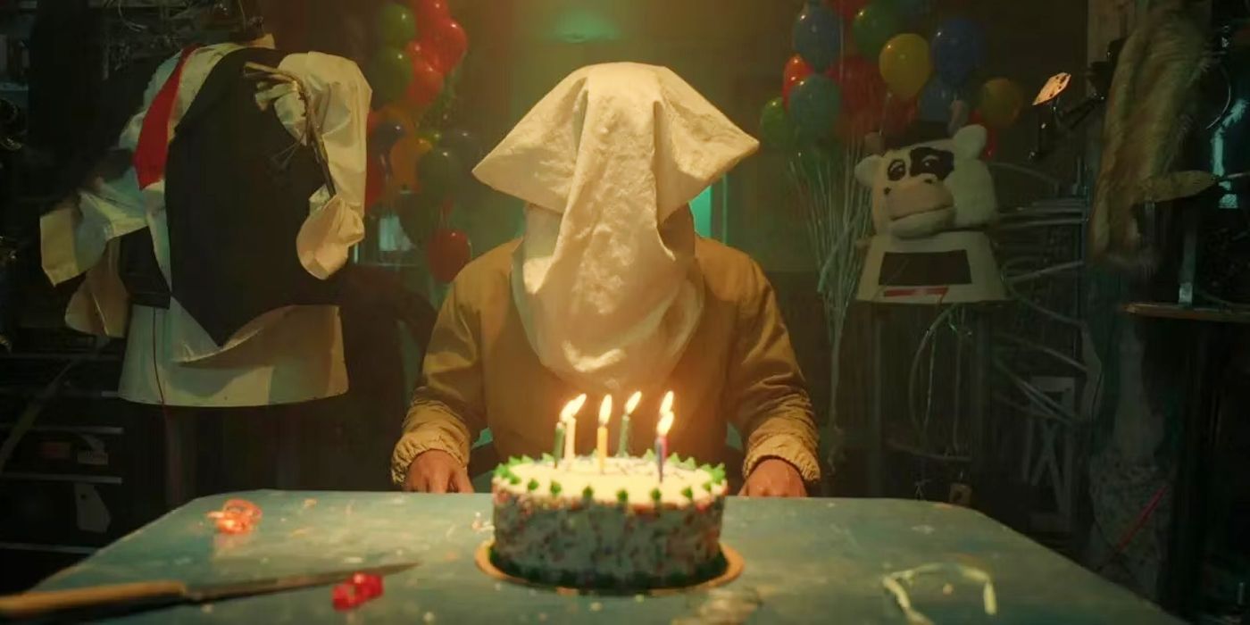 Them season 2 character with a bag over their head in front of a birthday cake